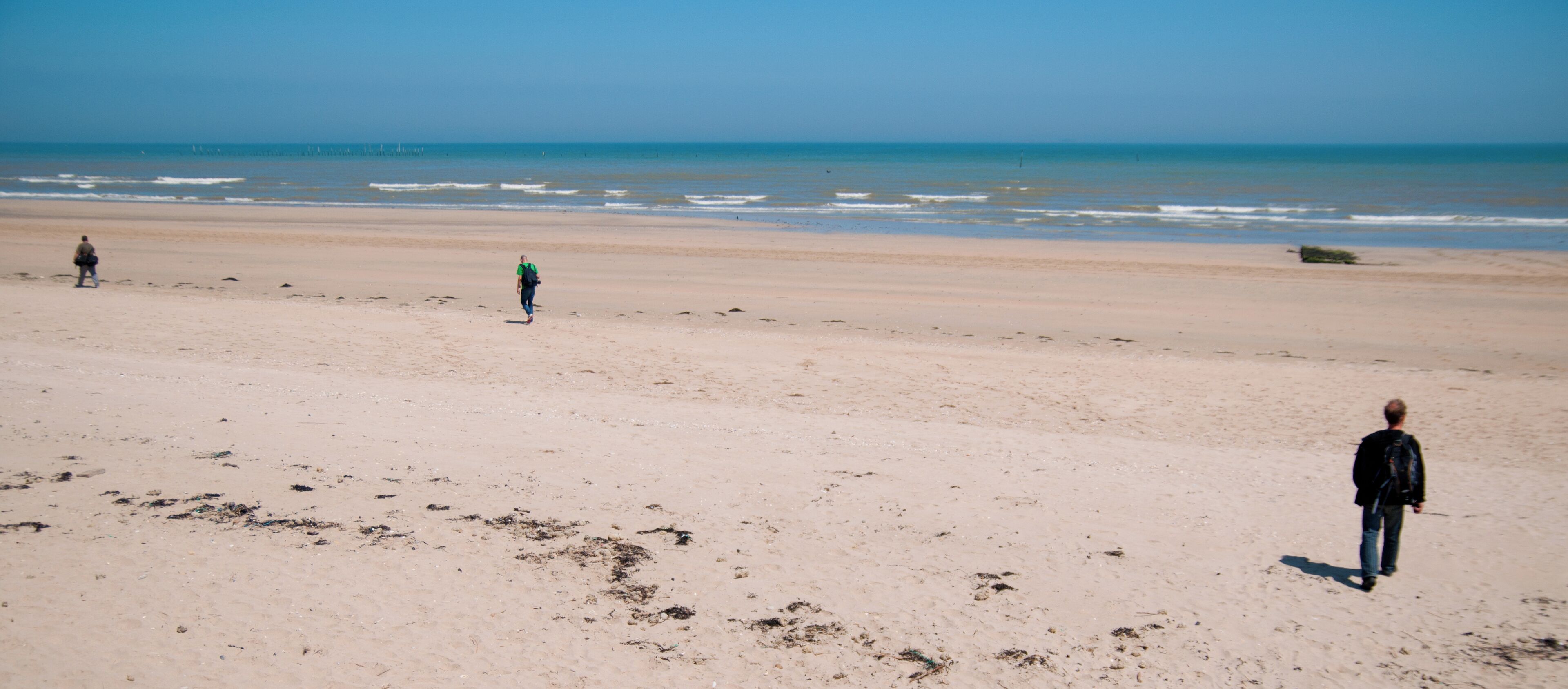 A sandy beach with footprints and a person walking towards the ocean.