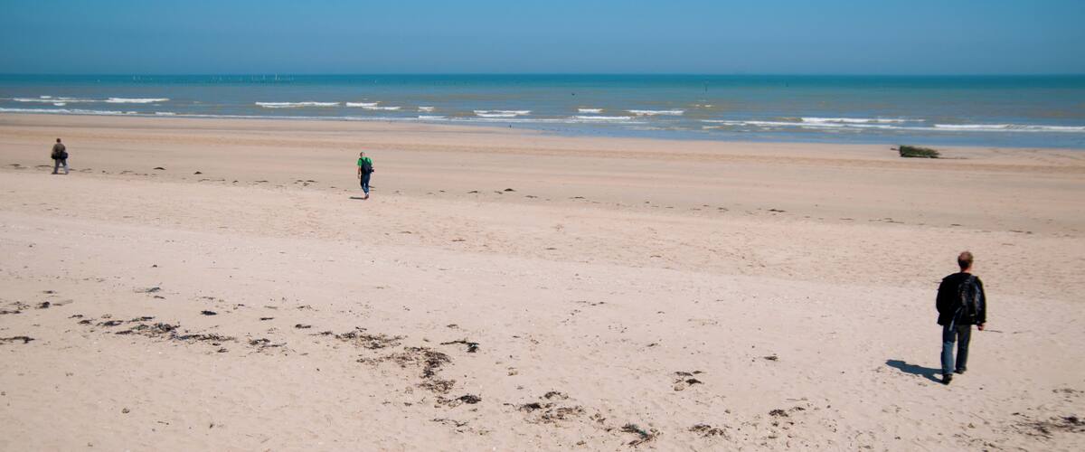A sandy beach with footprints and a person walking towards the ocean.
