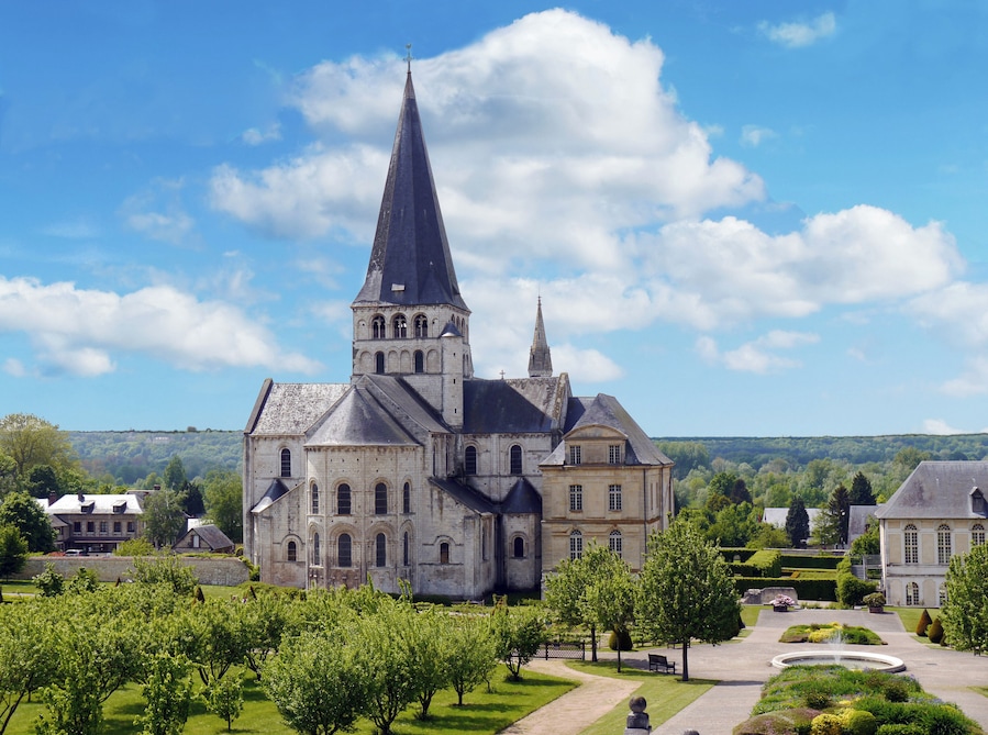 A historic church with a tall spire, surrounded by lush gardens and a clear blue sky.