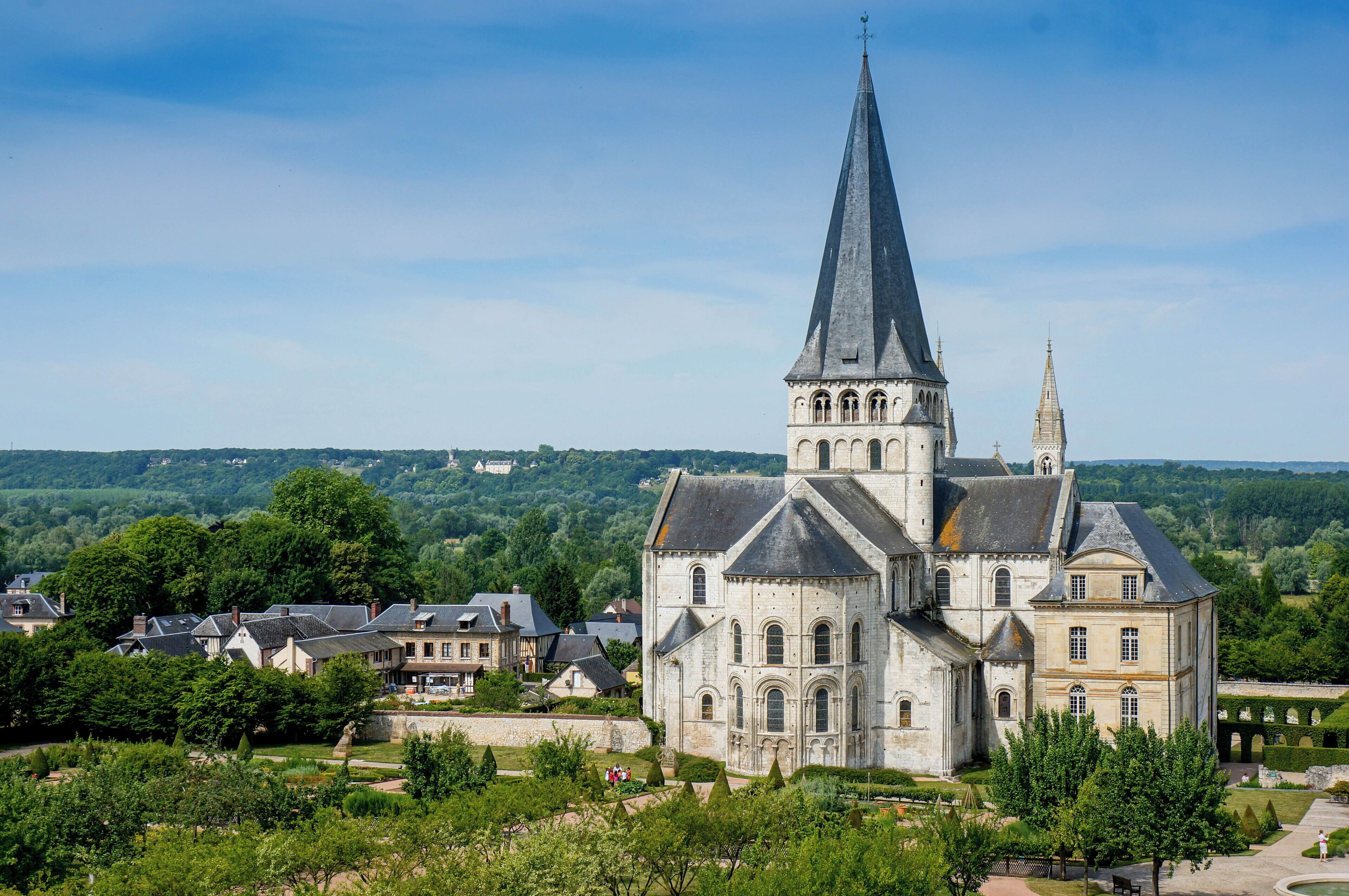 A historic church with a tall spire, surrounded by lush greenery and a village.