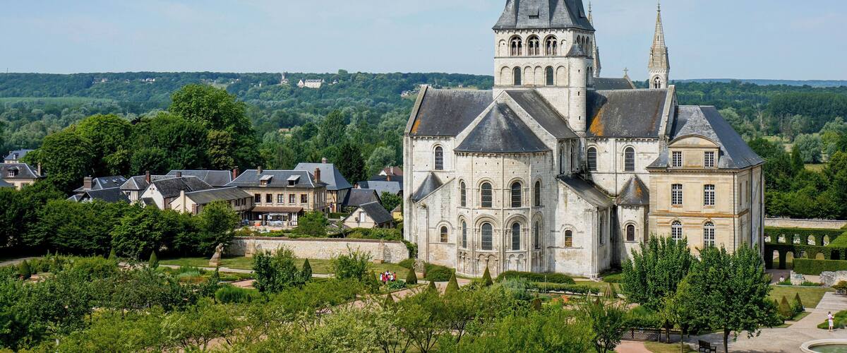 A historic church with a tall spire, surrounded by lush greenery and a village.