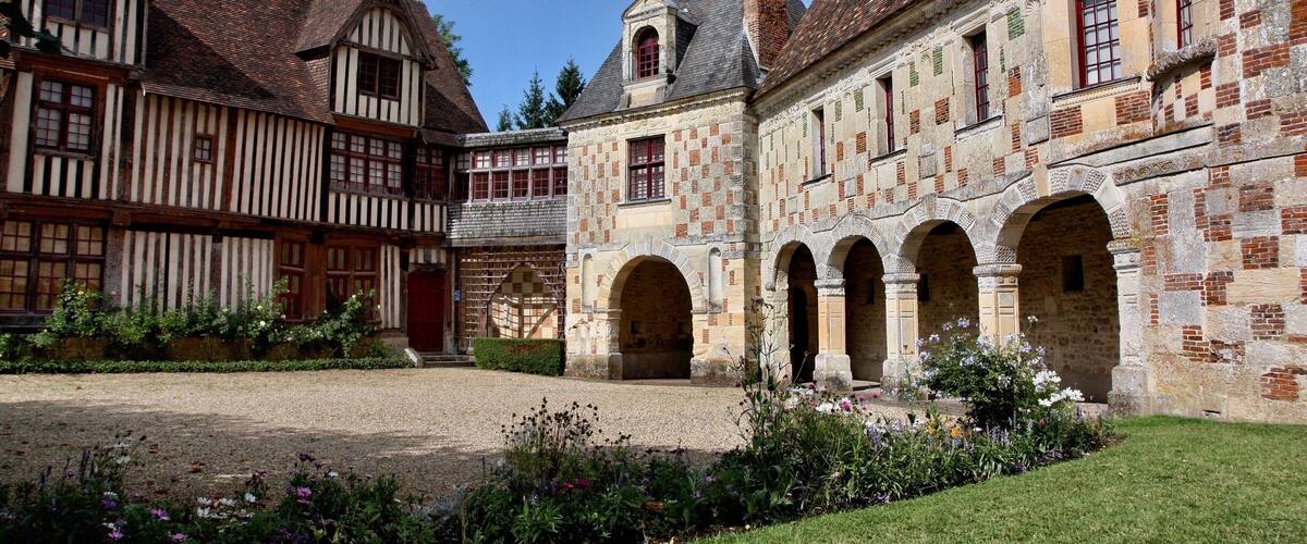 A courtyard with a cobblestone path, surrounded by historic buildings with timber framing and stone architecture.