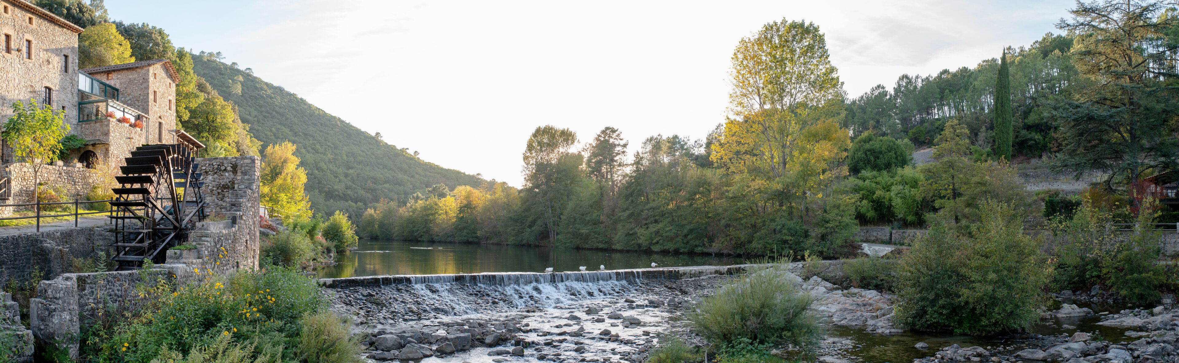 A stone bridge over a river, surrounded by lush greenery and a mountainous backdrop.