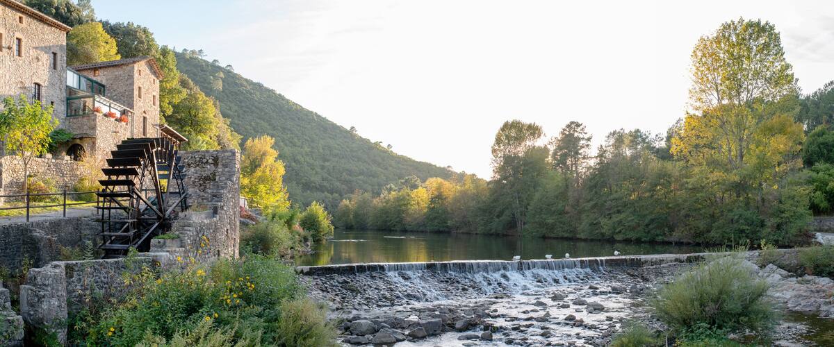 A stone bridge over a river, surrounded by lush greenery and a mountainous backdrop.