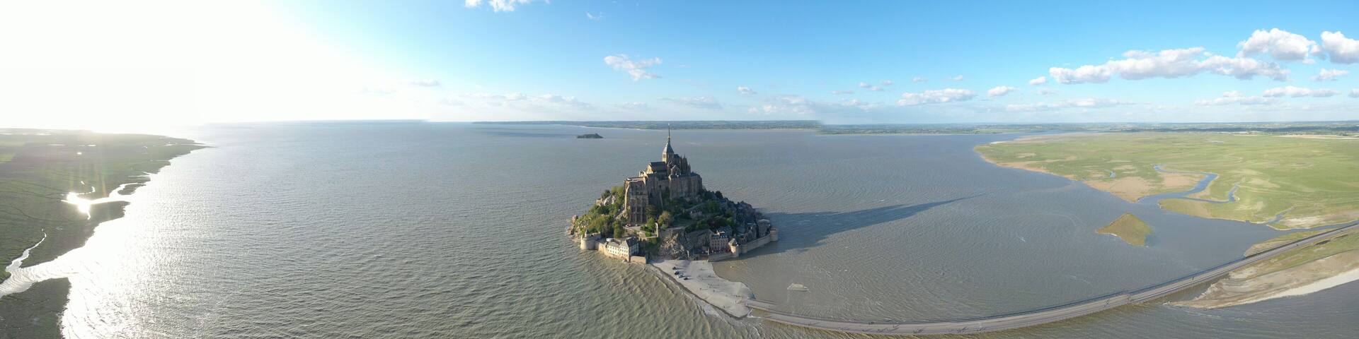 A coastal city with a prominent castle on a small island, surrounded by a large body of water and a bridge connecting to the mainland.