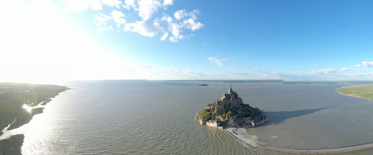 A coastal city with a prominent castle on a small island, surrounded by a large body of water and a bridge connecting to the mainland.