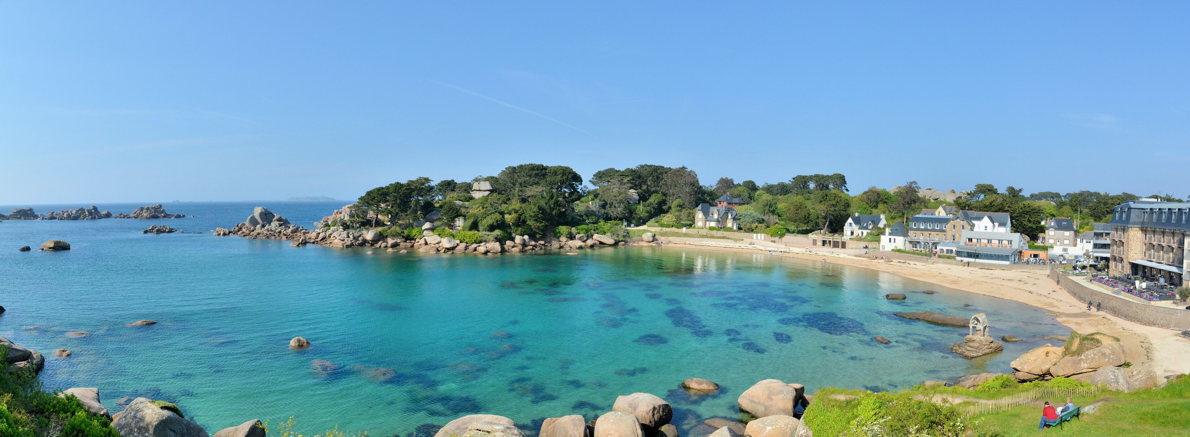 A coastal town with clear blue waters, rocky shoreline, and traditional buildings.