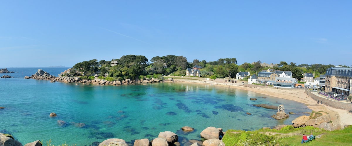 A coastal town with clear blue waters, rocky shoreline, and traditional buildings.