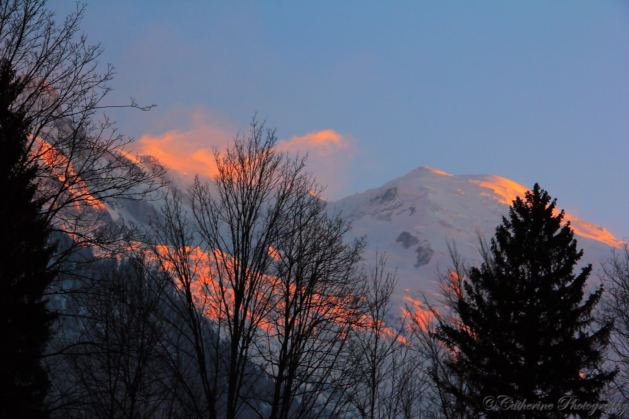 A mountain range with snow-capped peaks and a sunset sky.