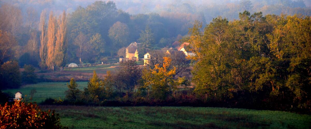 A misty landscape with a church surrounded by trees and fields.
