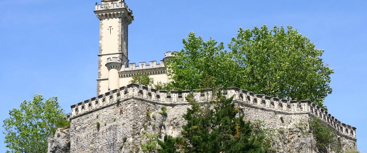 A historic stone castle with a prominent tower and a statue on top.