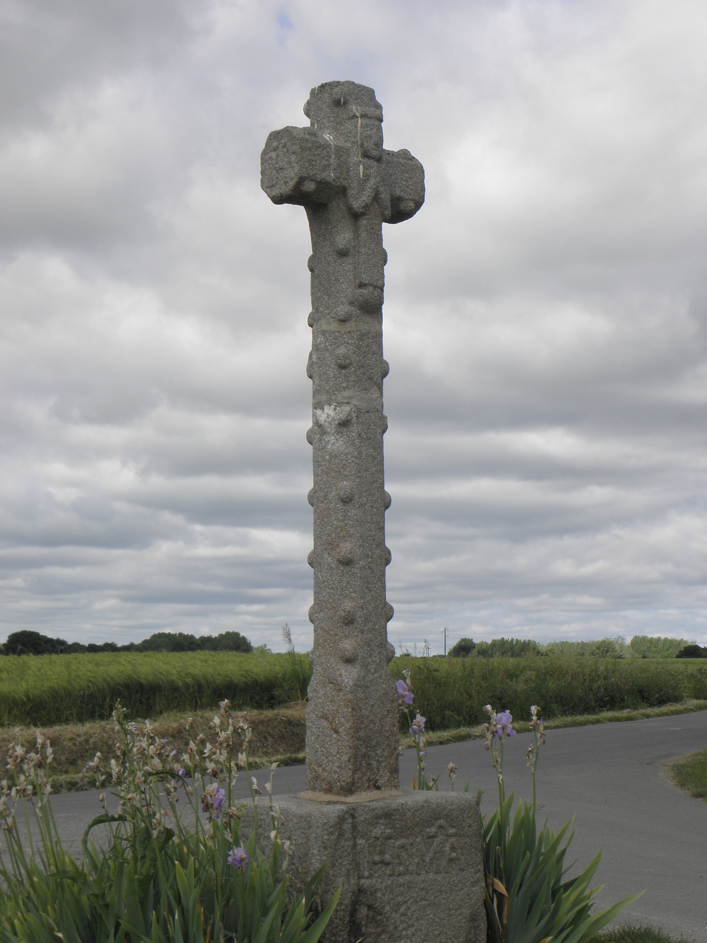 A stone cross in a rural setting with a cloudy sky.