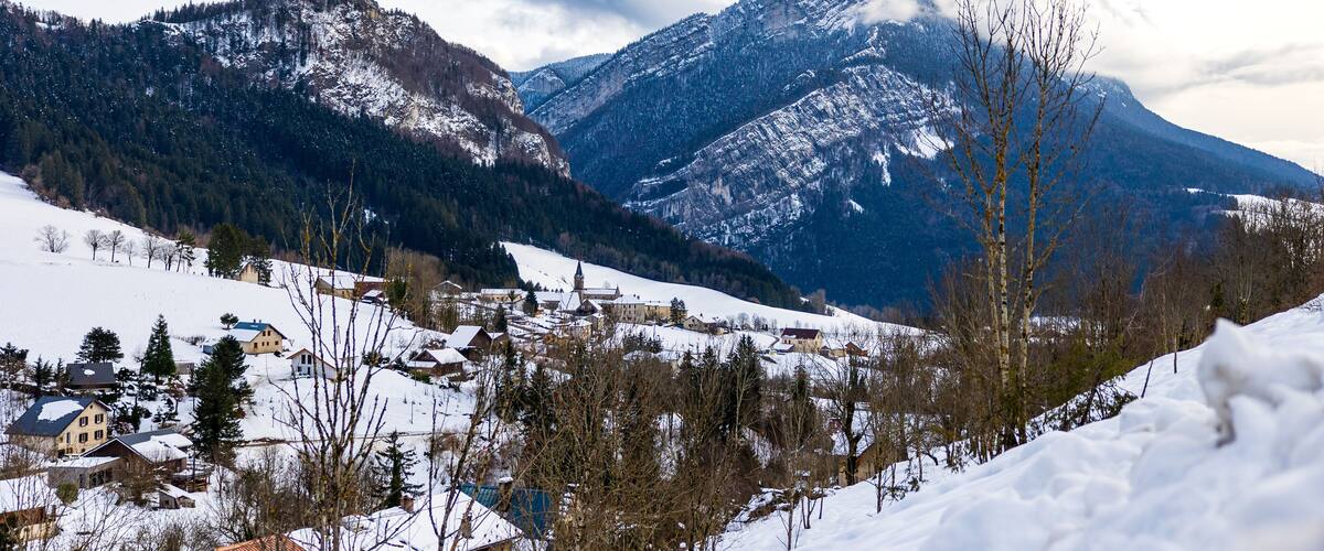 A snow-covered village with houses and a church, surrounded by mountains and trees.