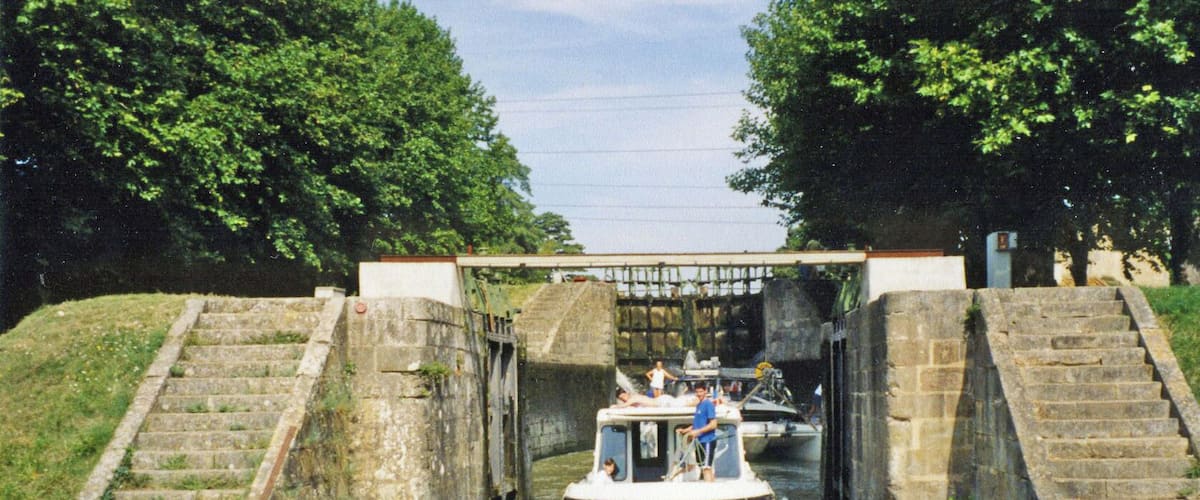 A narrow canal with a boat passing under a stone bridge.