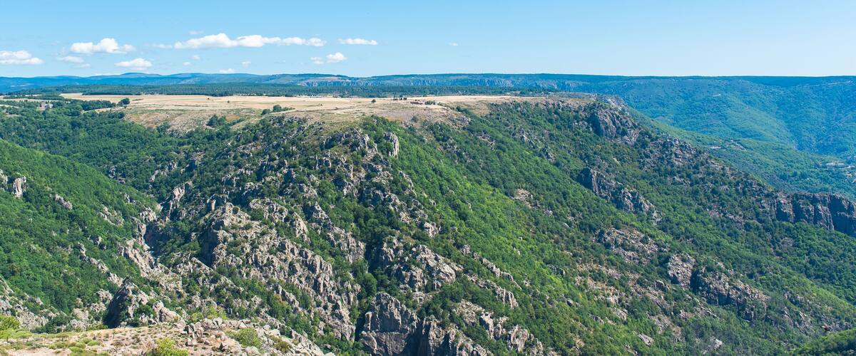 A mountainous landscape with dense green forests and rocky terrain.