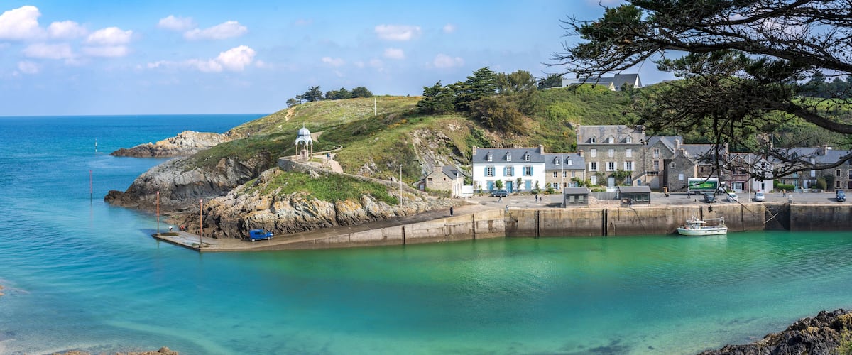 A coastal town with a lighthouse, rocky shoreline, and a harbor with boats.