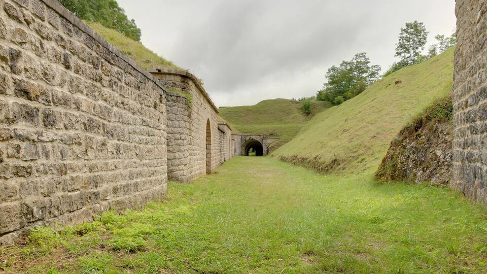 A stone wall with a tunnel entrance leading to a grassy hill.