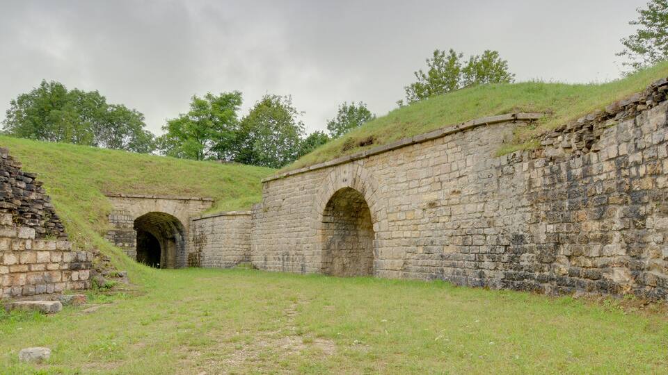 A historical stone structure with arched passageways and grassy terrain.