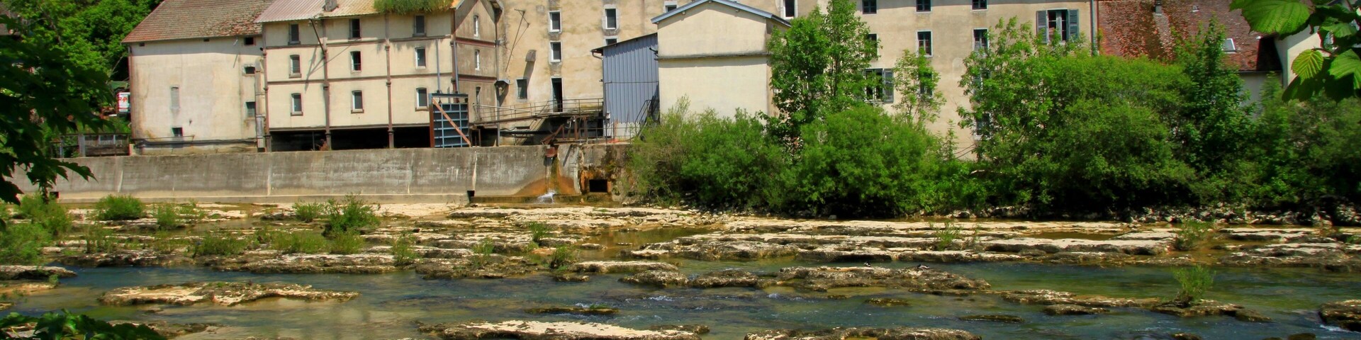A river with rocky terrain, a large industrial building, and surrounding greenery.