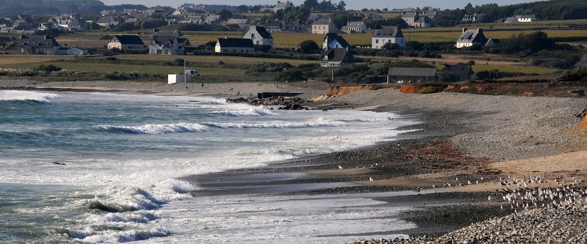 A coastal town with houses along the shore and waves crashing onto the beach.