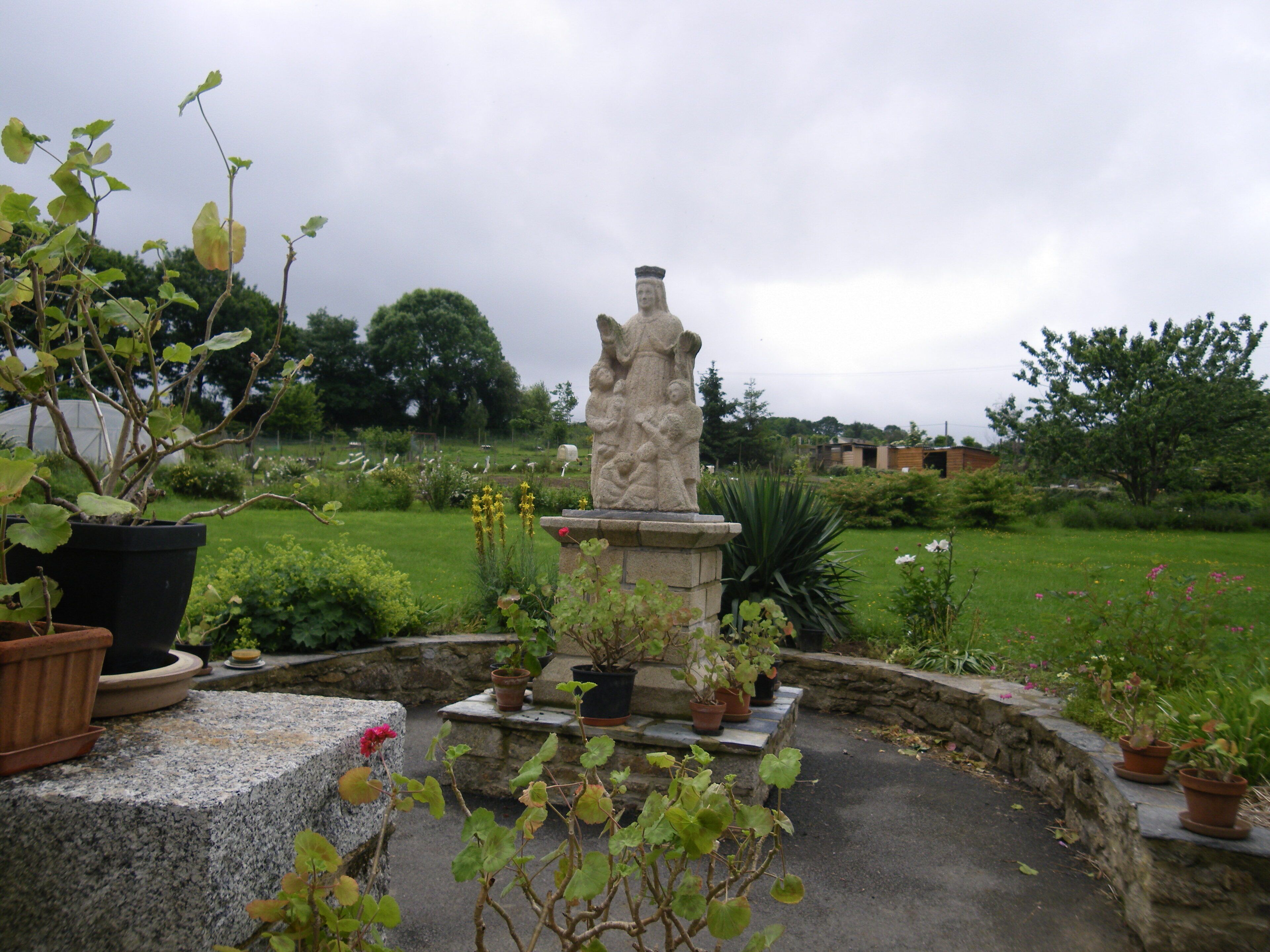 A garden with a statue, potted plants, and a grassy field.