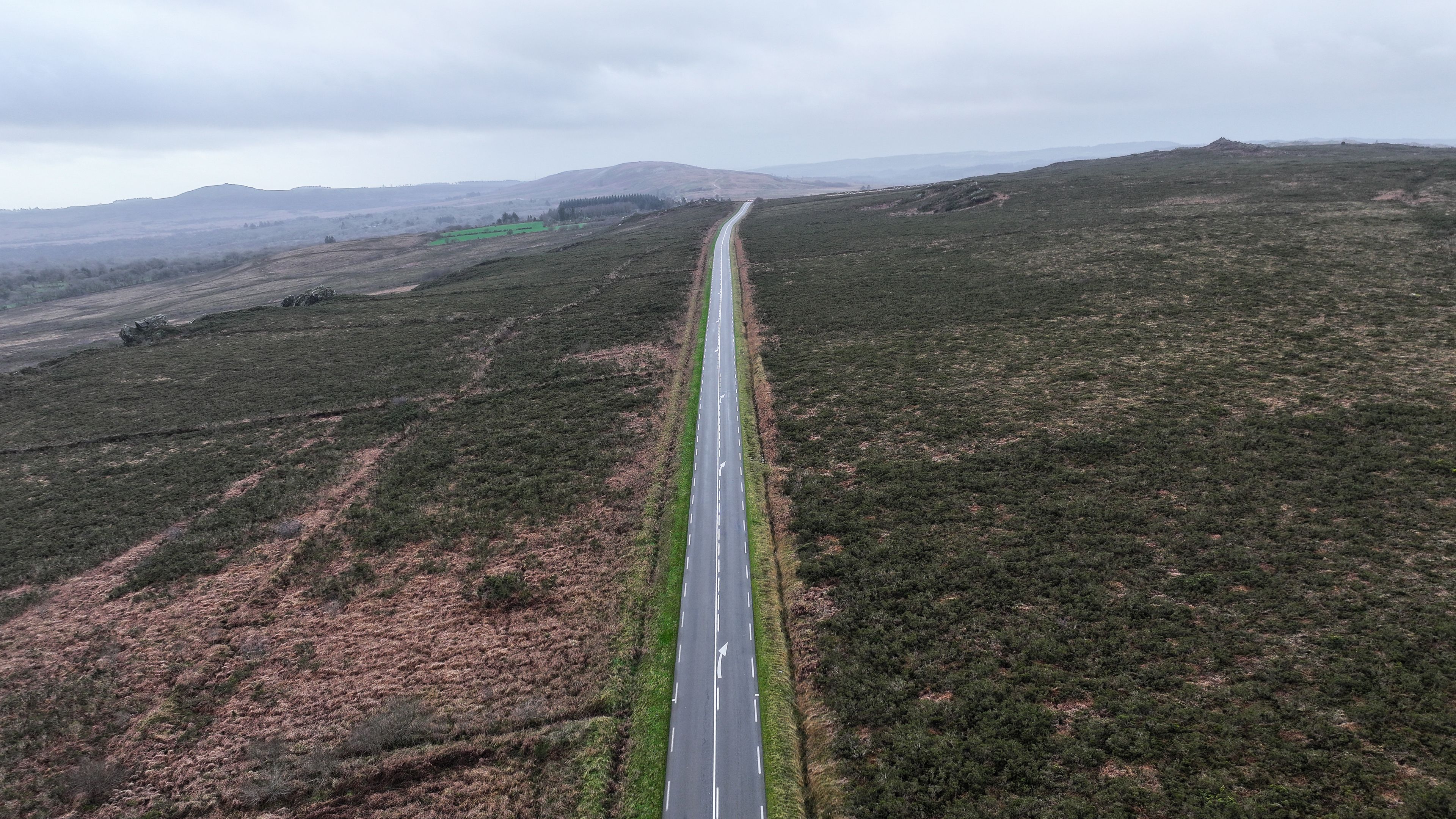 Aerial view of a straight road cutting through the moorland near Roc'h Trevezel under an overcast sky in Plouneour-Menez, Brittany, France.