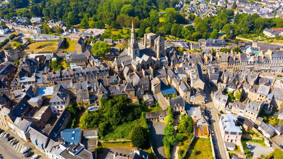 An aerial view of a historic town with a prominent church, narrow streets, and surrounding greenery.