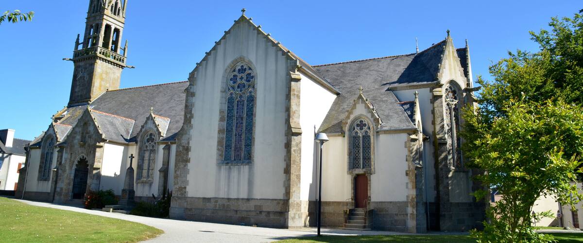 A historic church with a tall spire, large stained glass windows, and a well-maintained lawn.