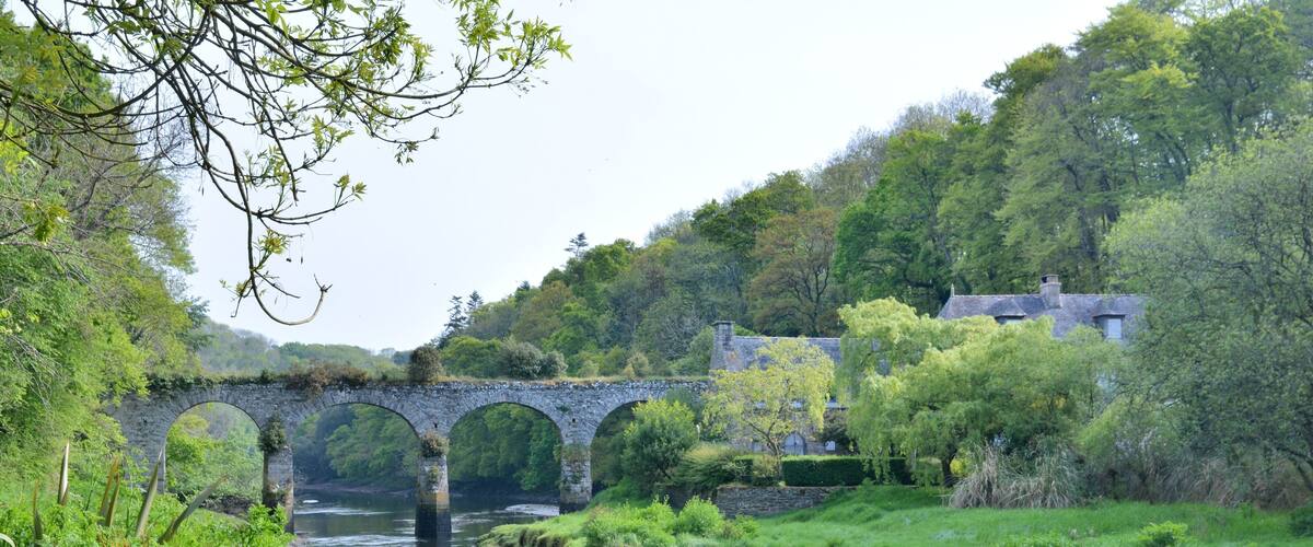 A stone bridge over a river, surrounded by lush greenery and trees.