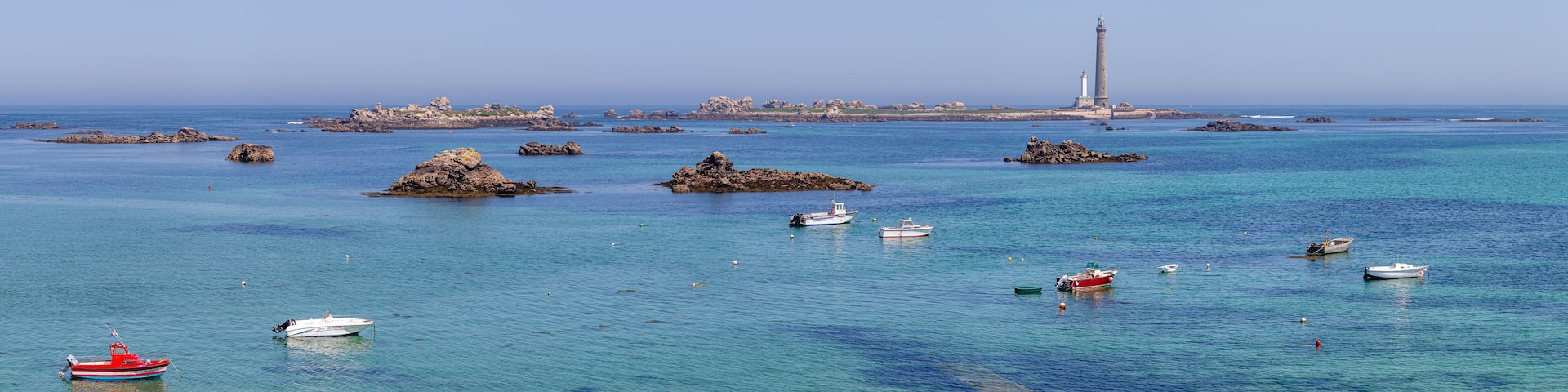 A coastal scene with a lighthouse, rocky outcrops, and several boats.