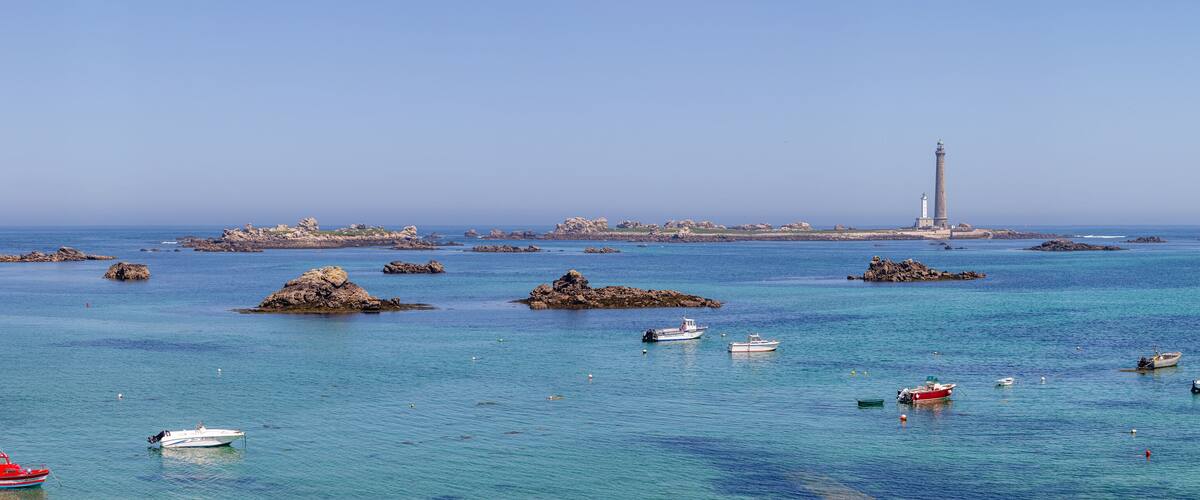 A coastal scene with a lighthouse, rocky outcrops, and several boats.