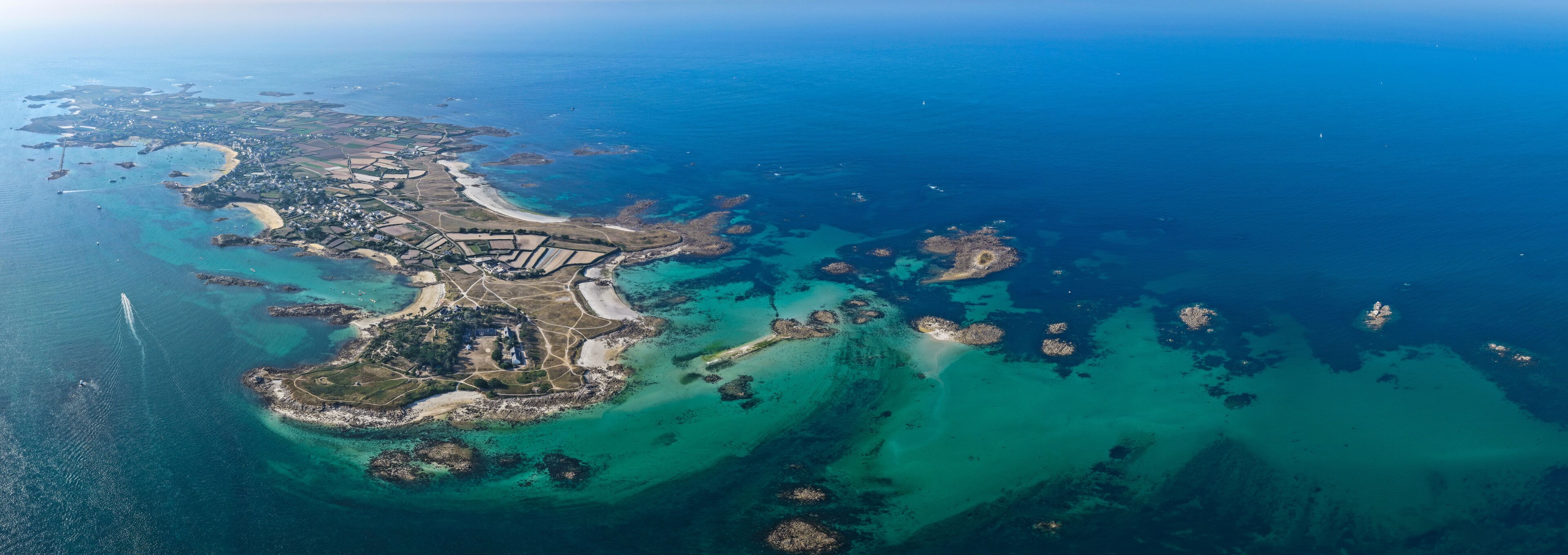An aerial view of a coastal area with a central island, surrounded by clear blue waters and smaller islets.