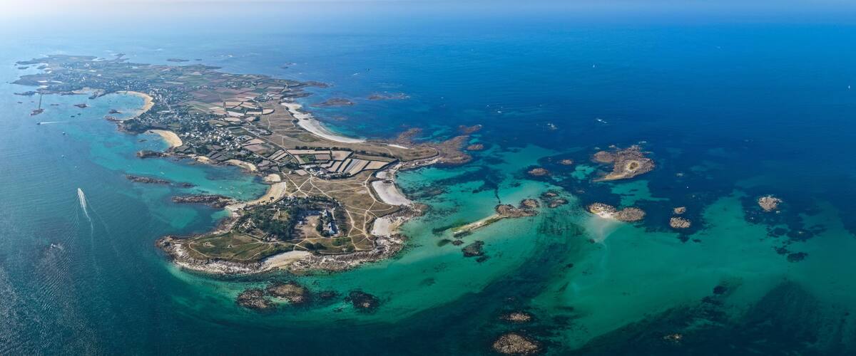 An aerial view of a coastal area with a central island, surrounded by clear blue waters and smaller islets.