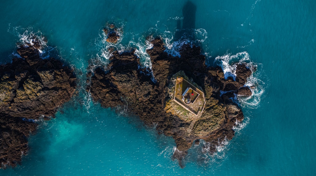 Aerial view of Phare de L'Ost-Pic lighthouse on a rocky islet with crashing waves and turquoise water in Plouezec, France.