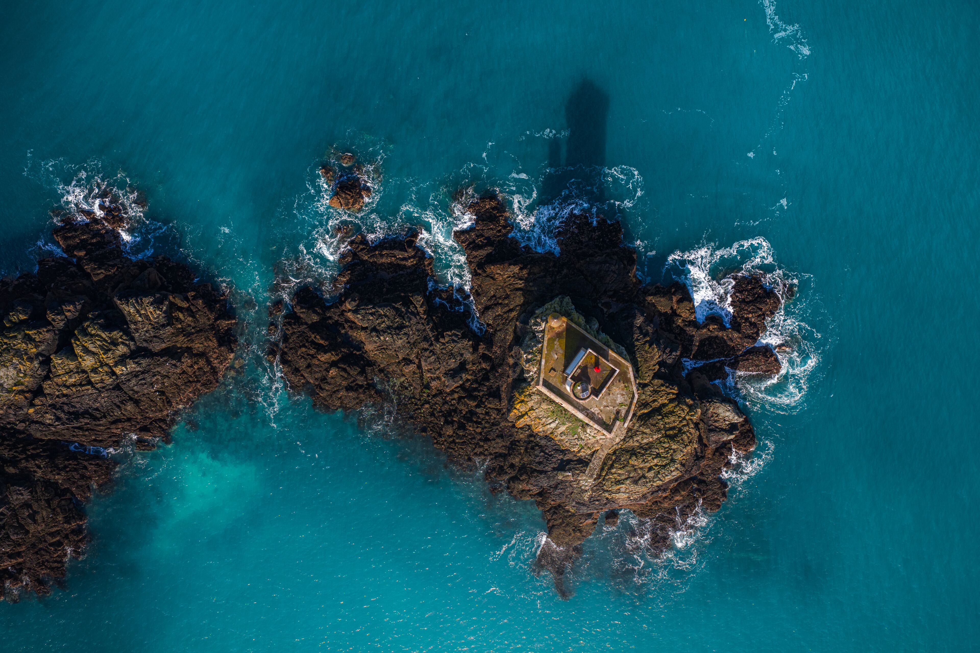 An aerial view of a rocky coastline with clear turquoise waters and a small boat anchored near the shore.