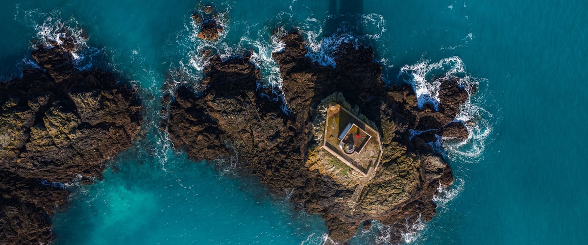 An aerial view of a rocky coastline with clear turquoise waters and a small boat anchored near the shore.