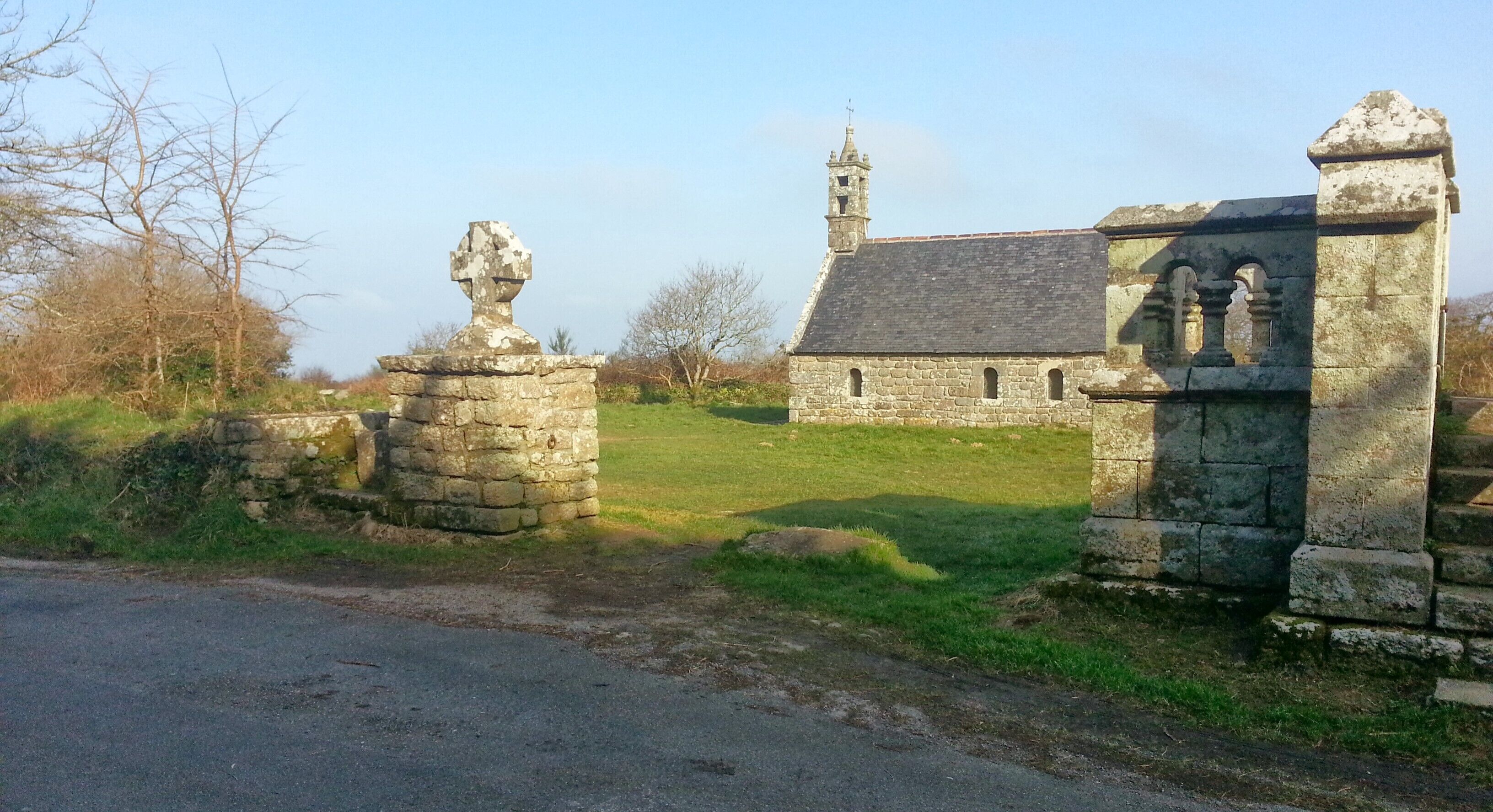 A stone church with a bell tower and a grassy field in the foreground.