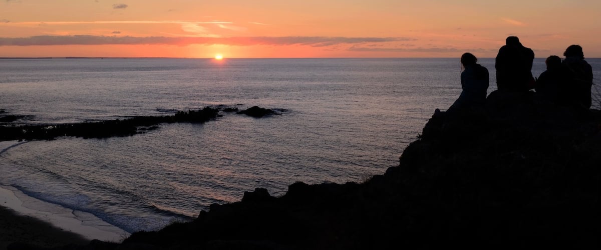 A sunset over the ocean with silhouettes of people on a cliff.