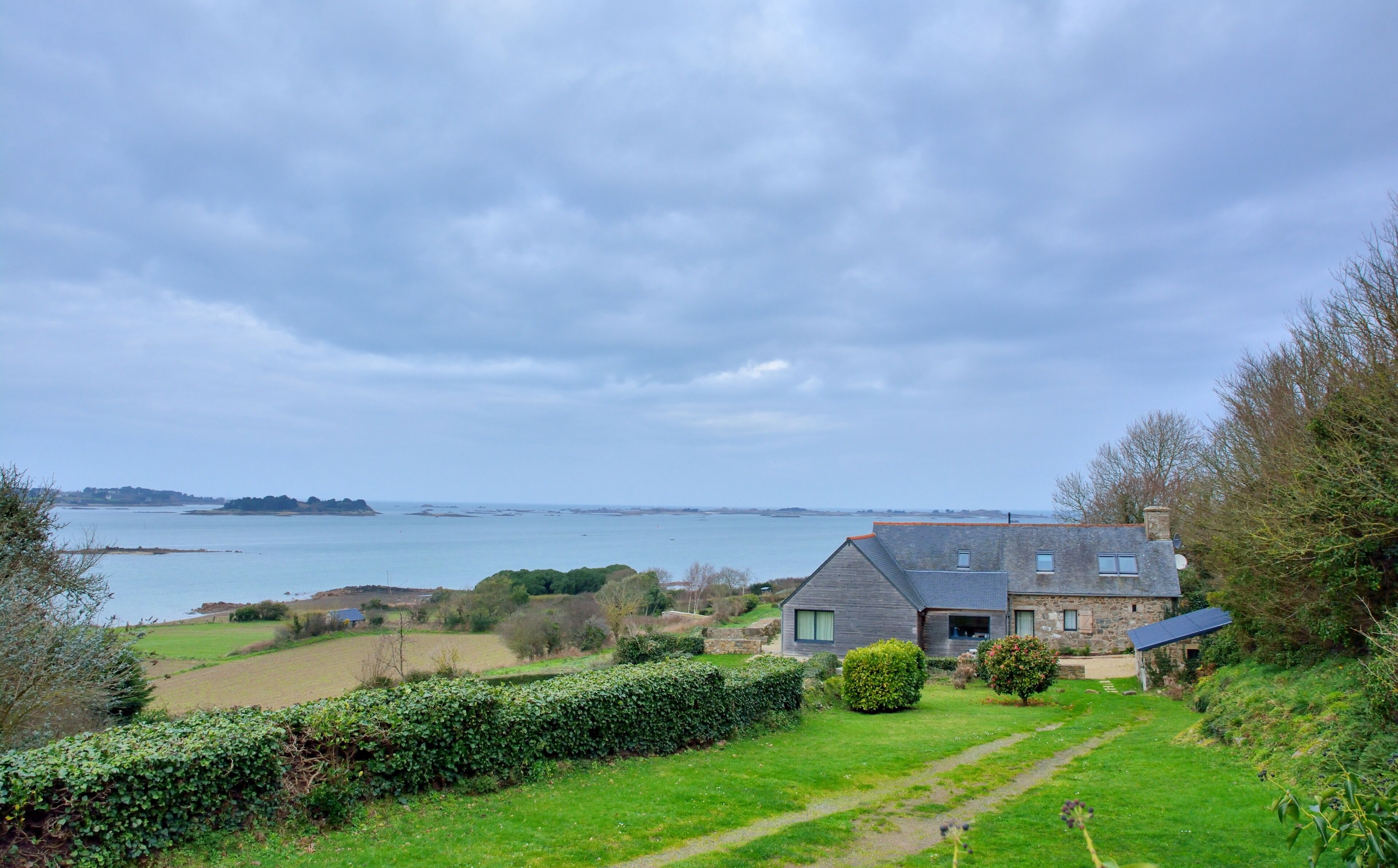 A coastal house with a view of the sea and distant hills.