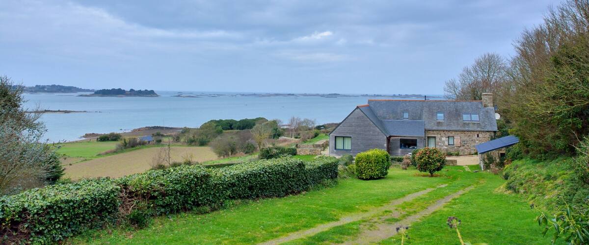 A coastal house with a view of the sea and distant hills.