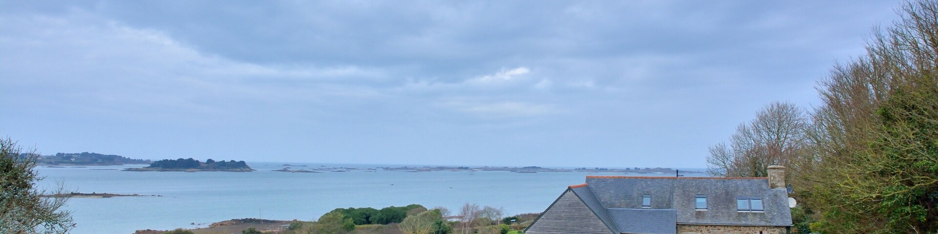 A coastal house with a view of the sea and distant hills.