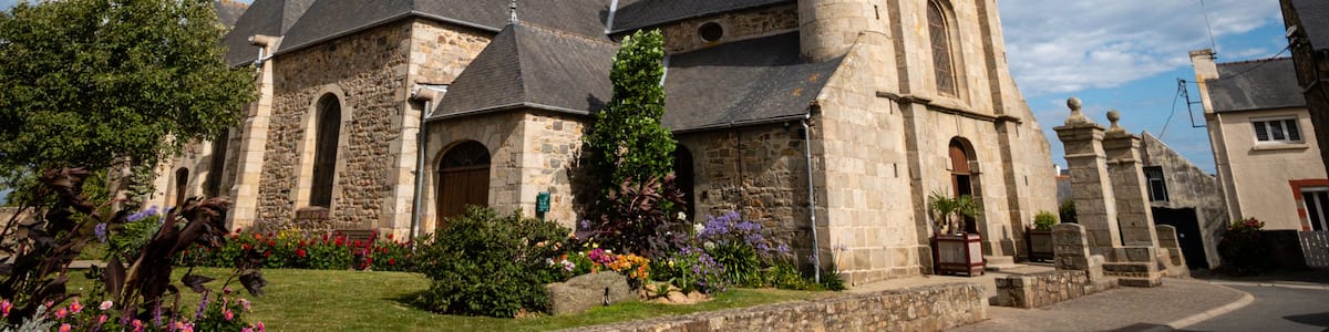 A historic stone church with a prominent bell tower, surrounded by well-maintained gardens and a clear sky.