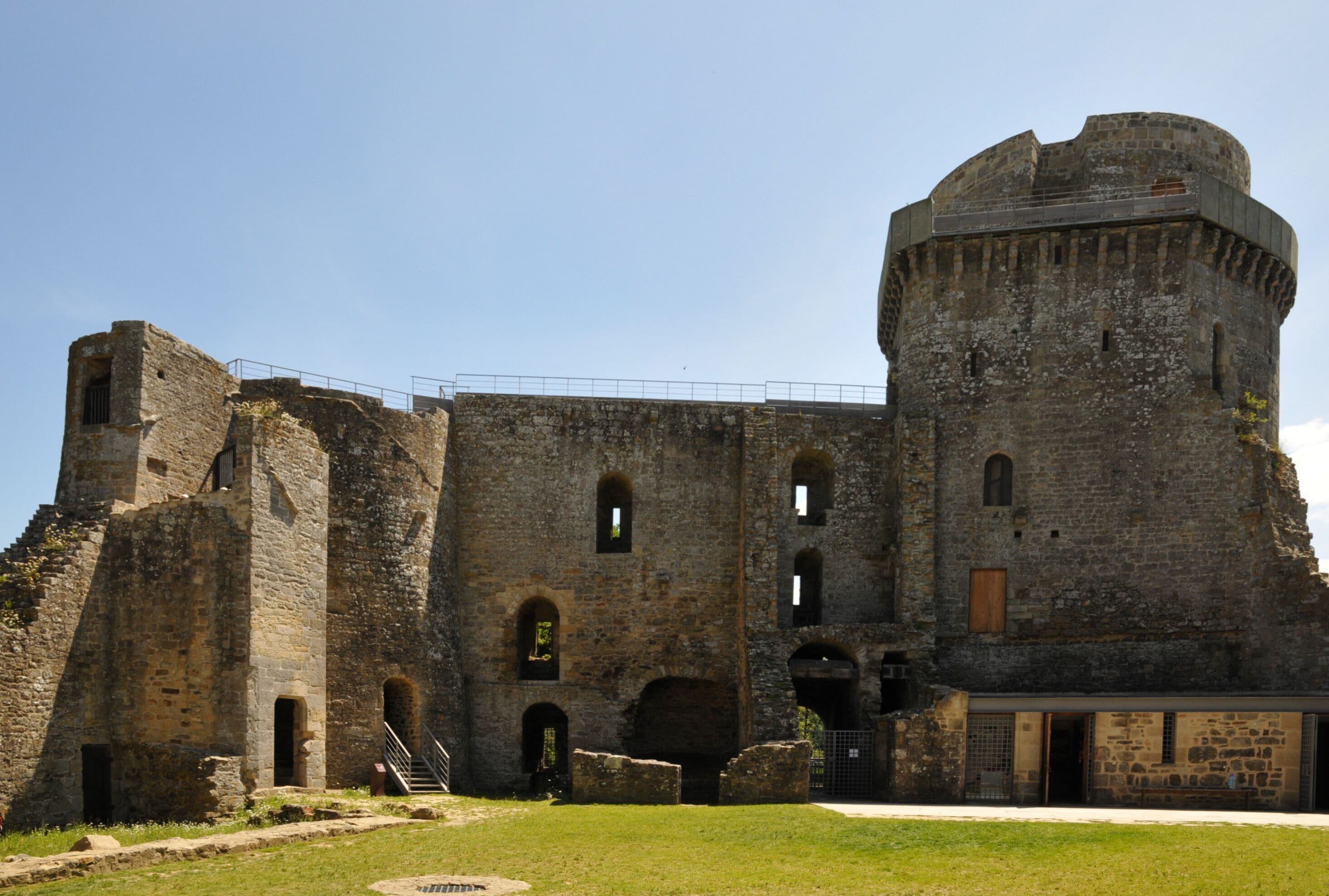 A historic stone castle with a round tower, arched windows, and a grassy courtyard.