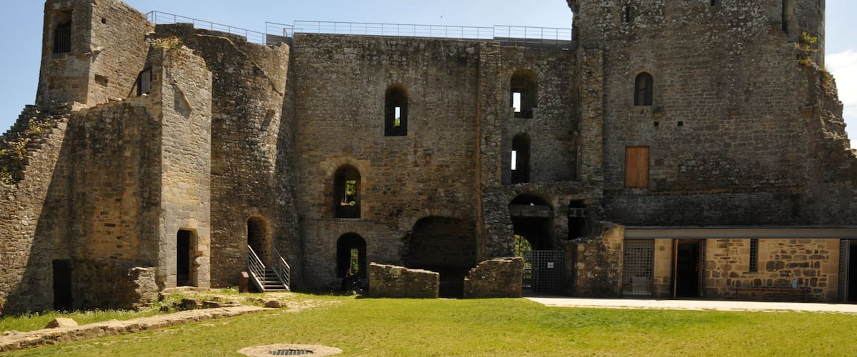 A historic stone castle with a round tower, arched windows, and a grassy courtyard.