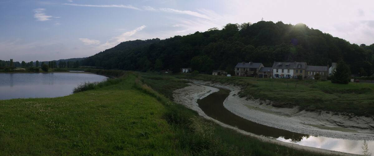 A calm lake surrounded by greenery, a small pavilion, and houses on a hillside.