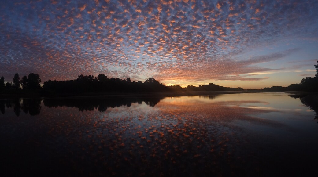 Un atardecer sobre un lago tranquilo, con la silueta de árboles y una colina distante.
