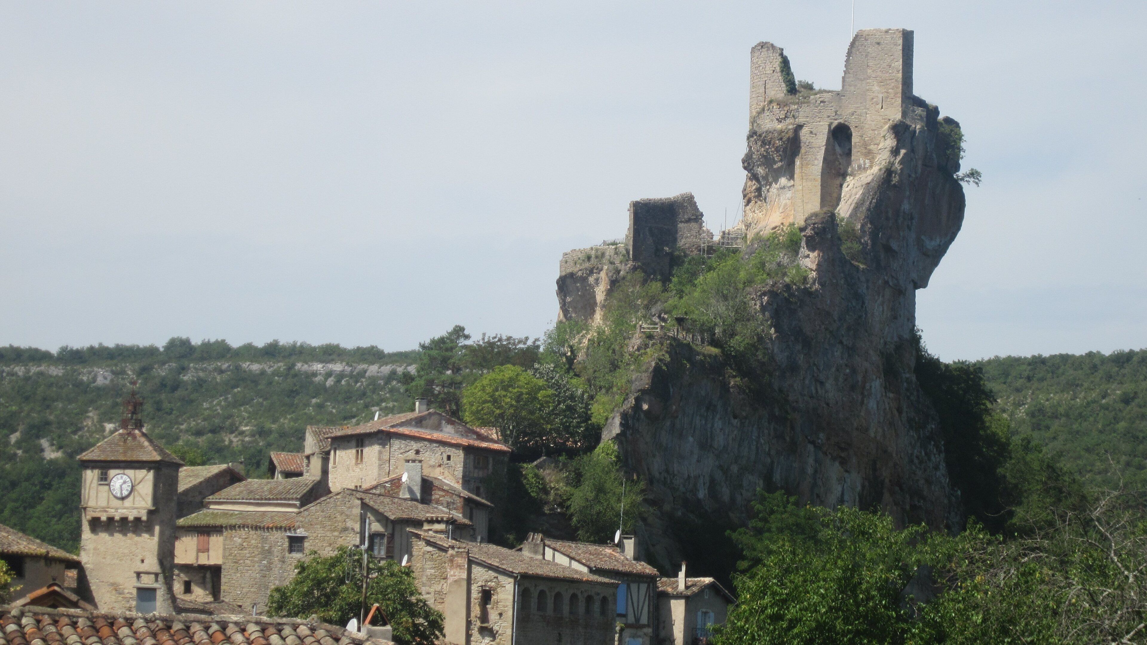 A medieval castle perched atop a rocky cliff, surrounded by traditional stone buildings with tiled roofs.