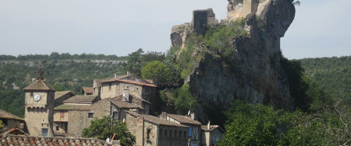 A medieval castle perched atop a rocky cliff, surrounded by traditional stone buildings with tiled roofs.