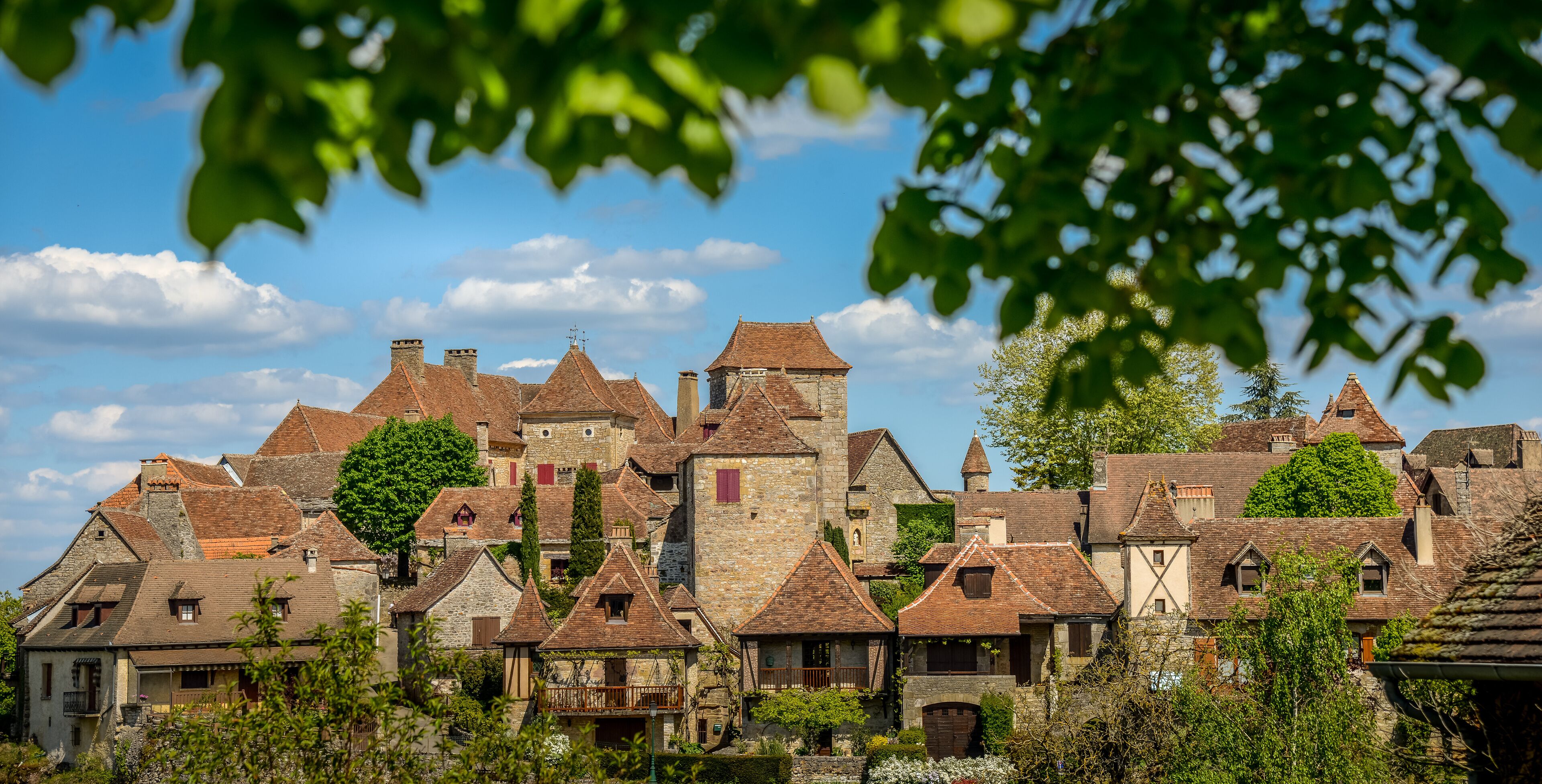 A historic village with stone buildings, red-tiled roofs, and a prominent tower.
