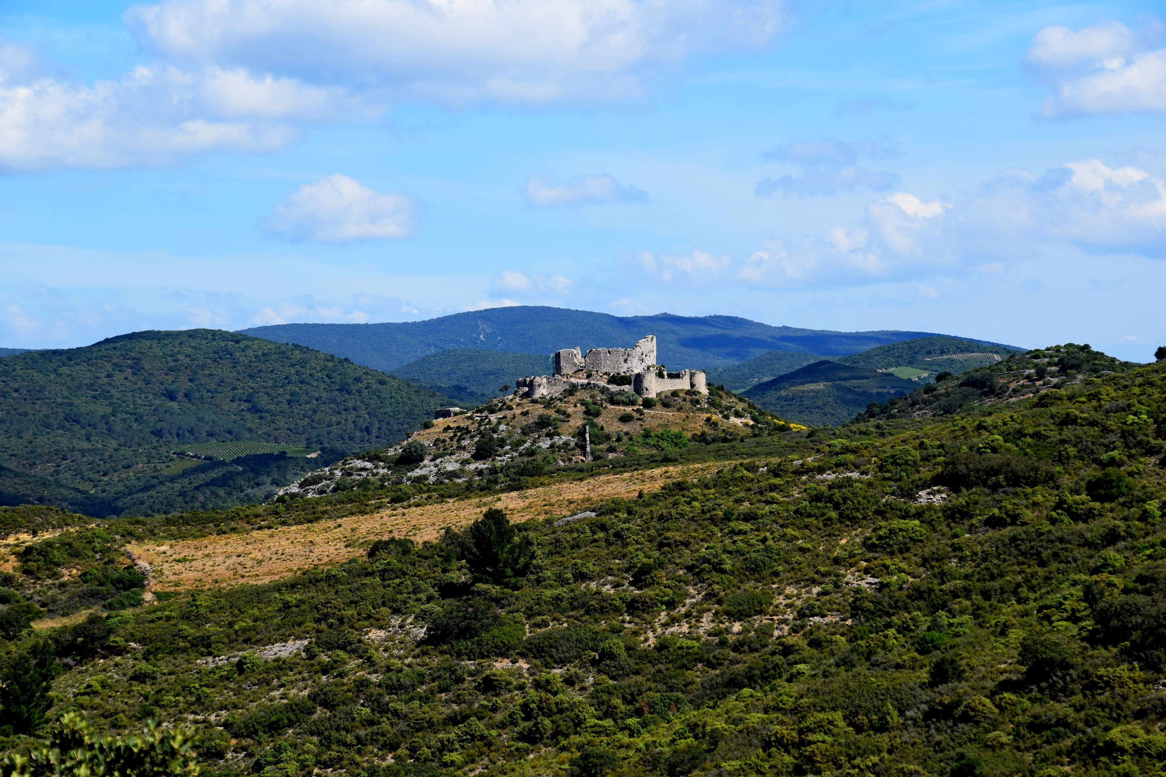A castle on a hill surrounded by lush green hills and a clear blue sky.